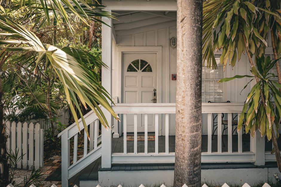 The inviting front porch of an elegant Southern home, featuring a classic wooden door and gas lanterns, illuminated by warm evening light.